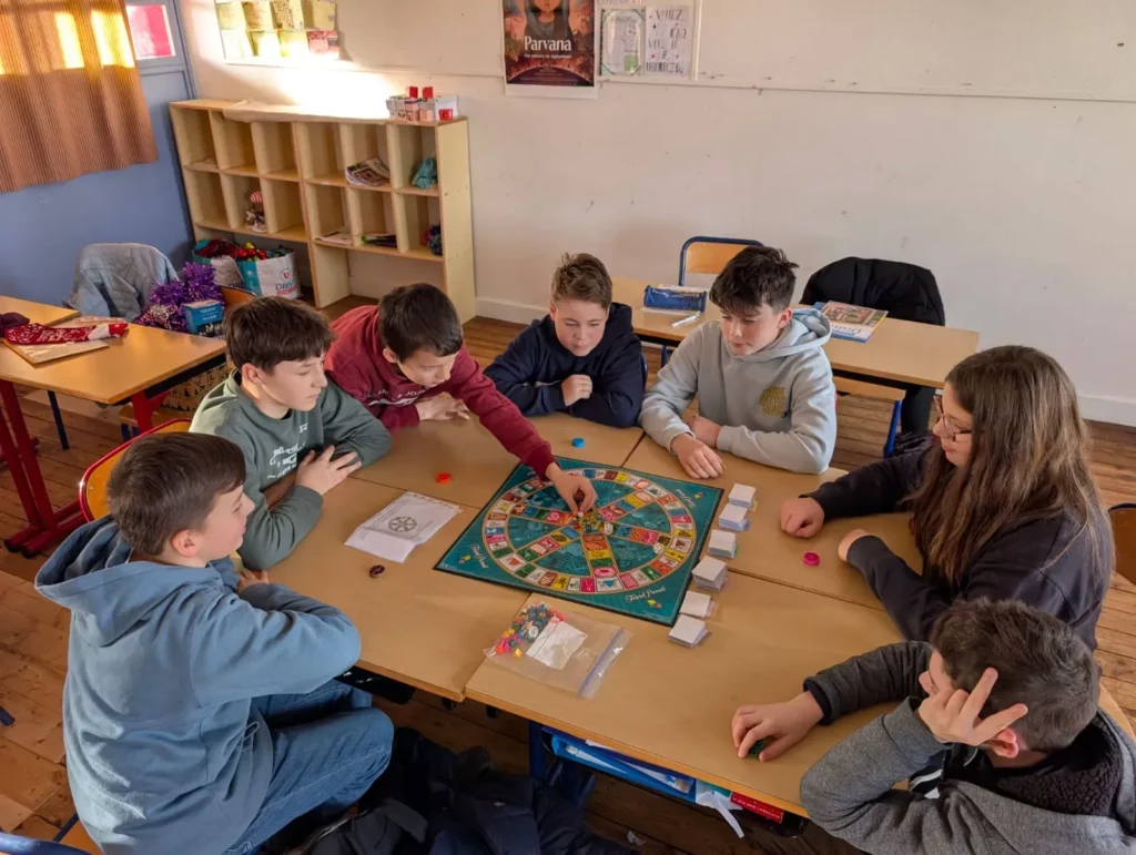 Un groupe d'élèves joue calmement à un jeu de société dans une salle de classe lumineuse.