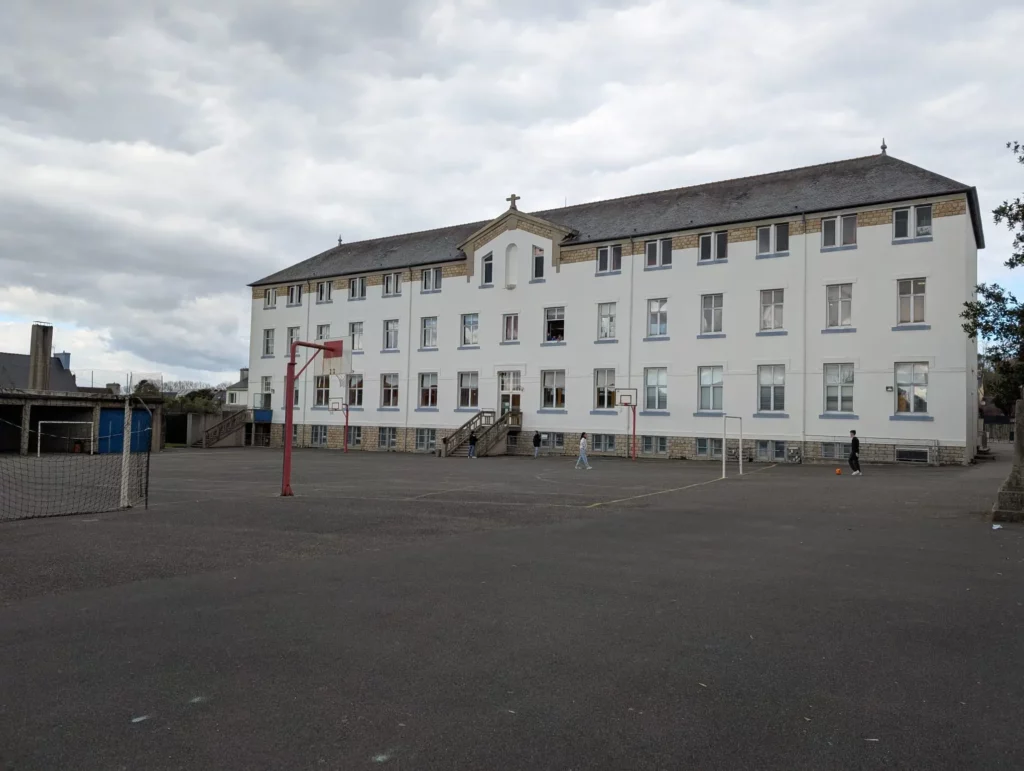 Façade du collège La Mennais Cap Sizun, grand bâtiment rectangulaire sous un ciel nuageux.