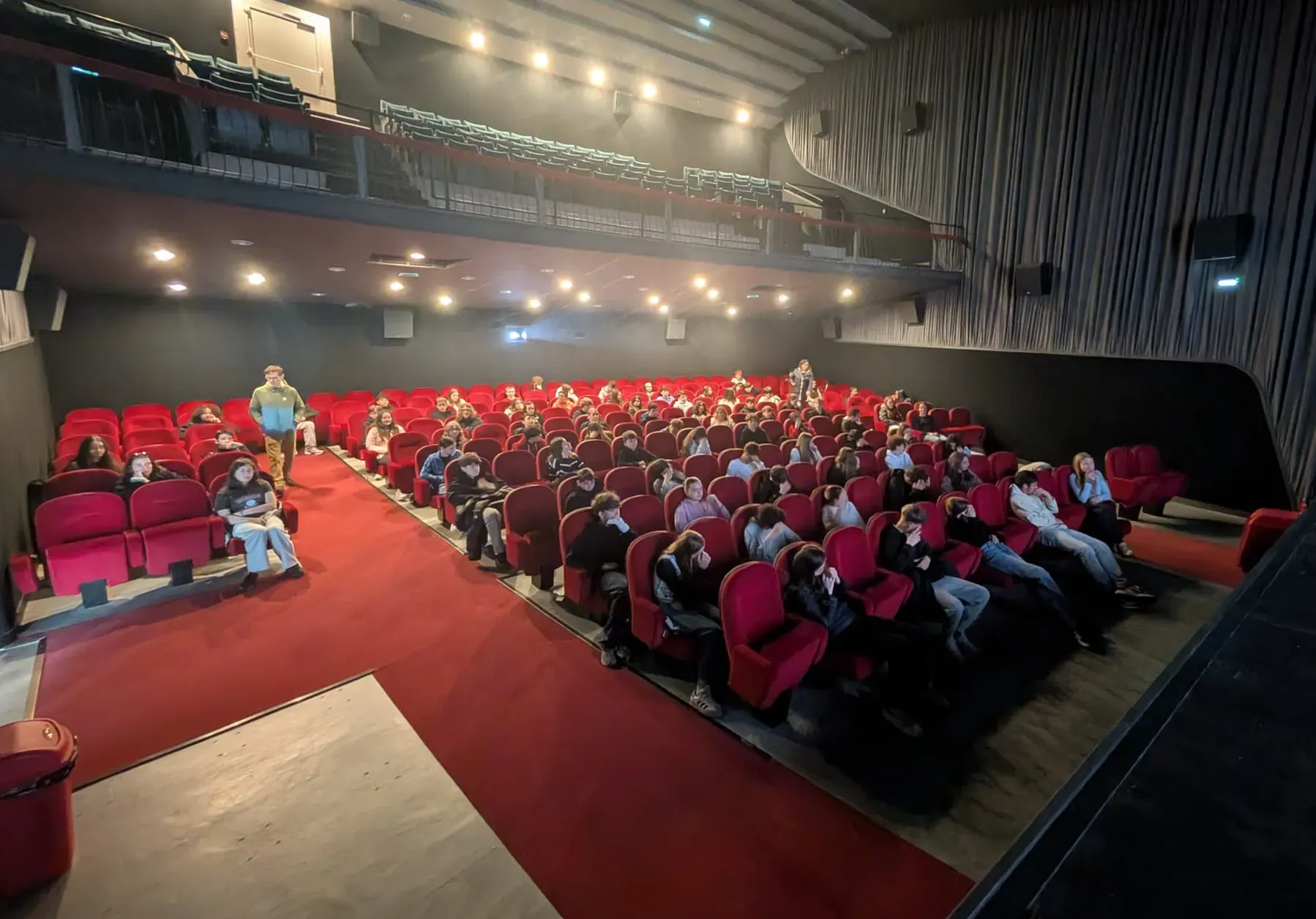 Salle de cinéma vue depuis les gradins, élèves installés dans les fauteuils rouges.