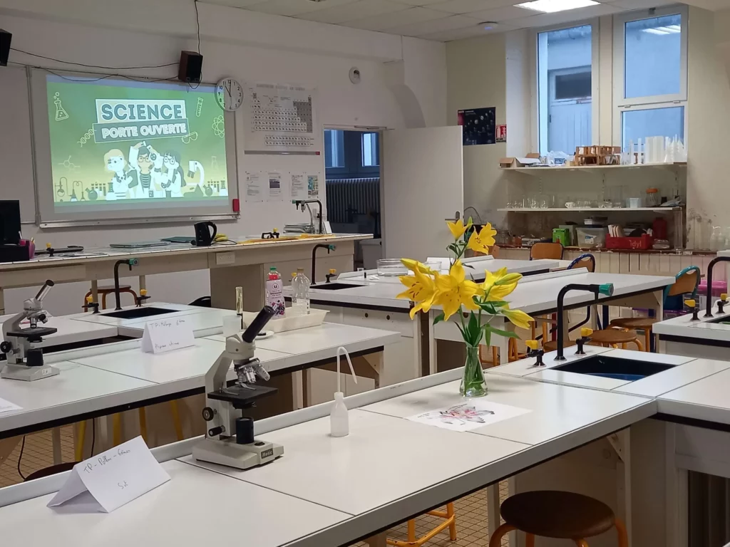 Salle de sciences avec paillasses, microscopes et projecteur allumé en fond.