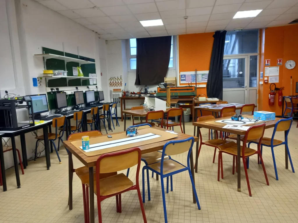 Salle de technologie avec tables de travail, chaises et tableau interactif, sans élèves.