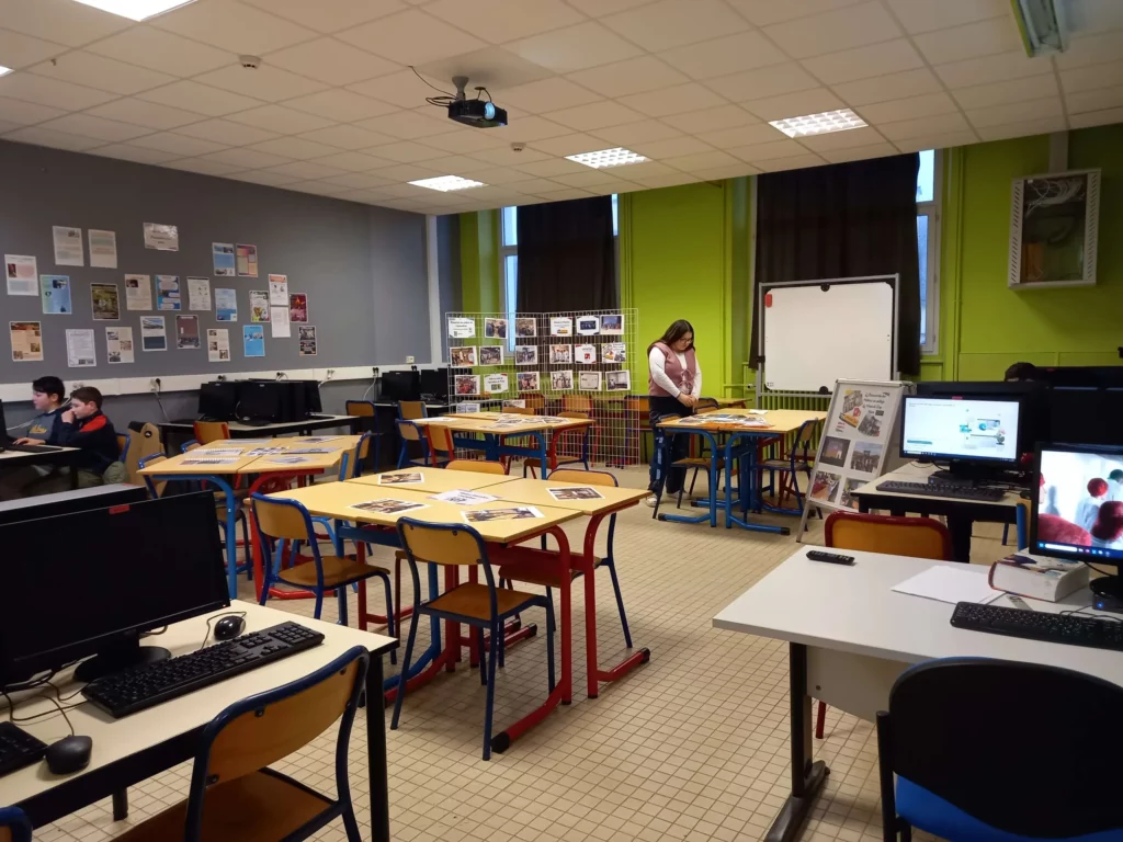 Salle informatique avec ordinateurs sur tables, murs verts, lumineuse et quelques élèves qui y travaillent.