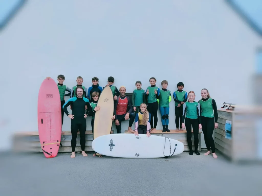 Classe entière posant avec des planches de surf devant un bâtiment.