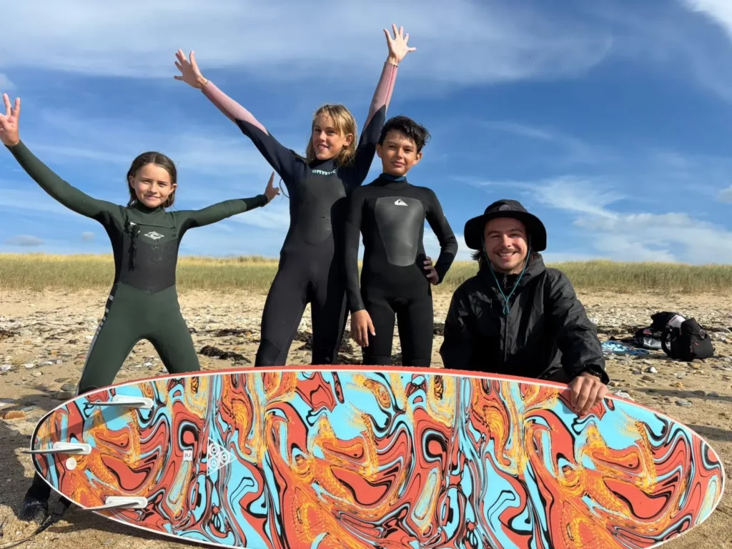 Groupe d'élèves en combinaison de surf sur la plage, bras levés.
