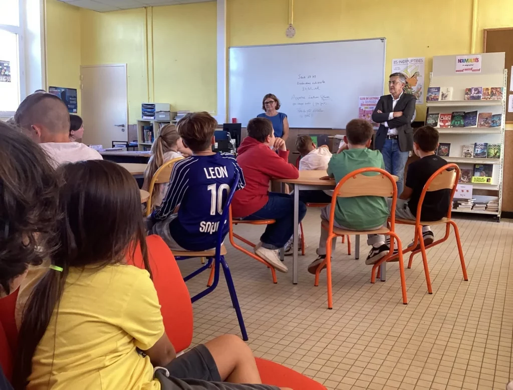 Élèves assis à leur table et écoutant Didier Guillon, conseiller départemental, venu remettre l'ouvrage et échanger avec eux.
